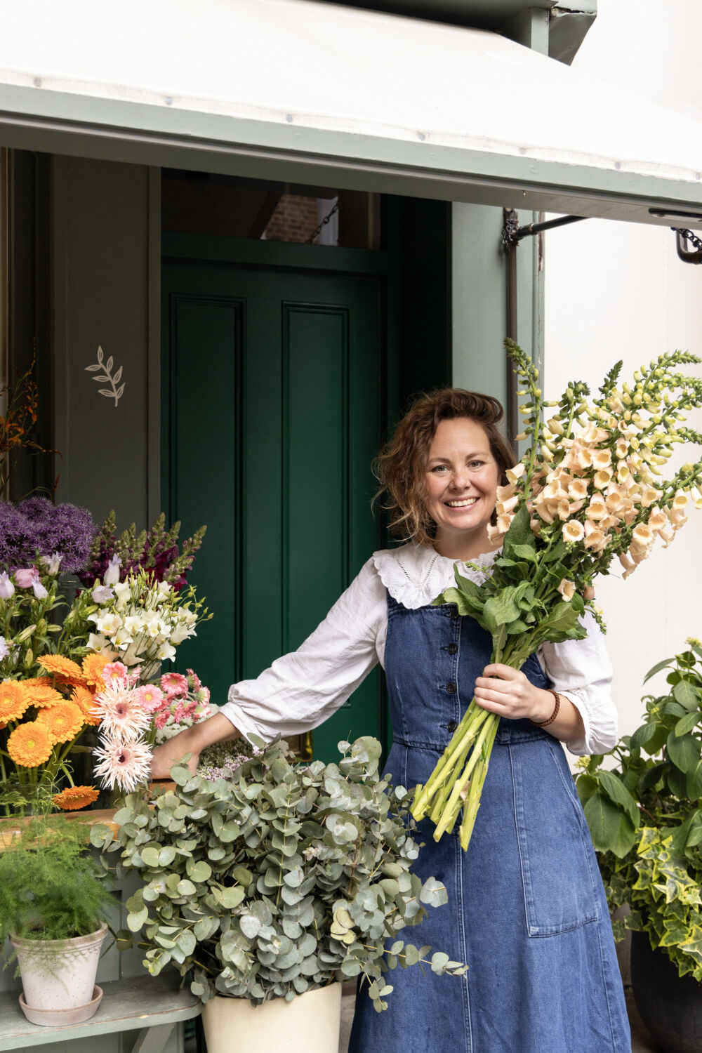 Alice, founder of Botanique Workshop, stood outside her florist in London holding a bouquet of british flowers